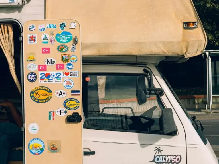 The side of a white RV covered in colorful travel stickers.