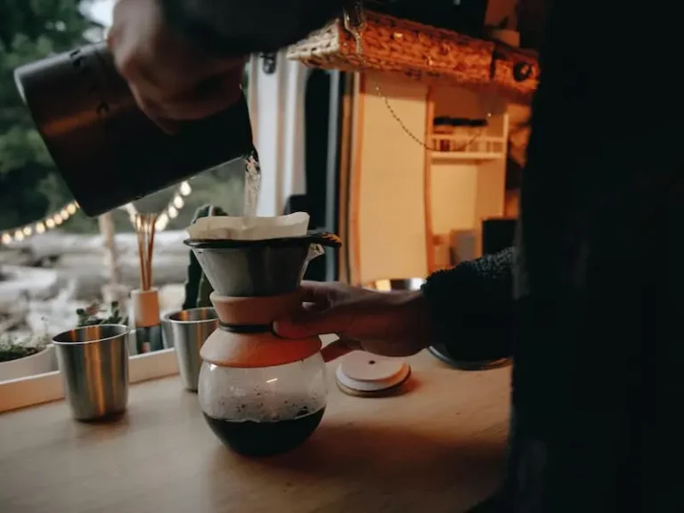 Close-up shot of a person brewing coffee with a pour-over dripper in a vintage camper van.