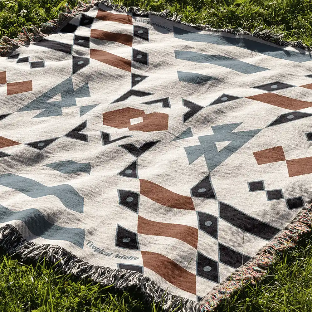 A close-up shot of the Wandering Warrior Blanket laid out on green grass, highlighting its intricate blue, brown, and black geometric pattern and textured weave.