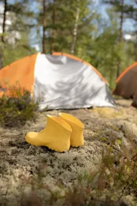 Children's yellow boots placed outside an orange tent during a family camping trip in the woods.