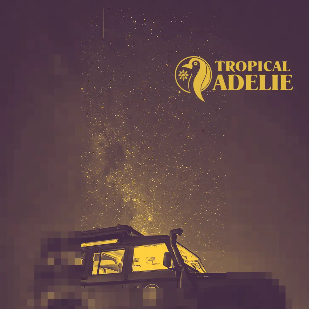 An off-road vehicle glows with a warm yellow light from within, parked under a vast, star-filled night sky and the Milky Way. The image features a purple and gold duotone aesthetic with the "Tropical Adelie" logo in the top right corner.