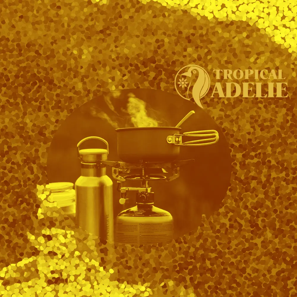 A small portable camping stove with a metal pot on top, emitting steam. A stainless steel water bottle stands next to it. The entire scene is filtered in gold and framed by a circular cutout over a shimmering mosaic background. The 'Tropical Adelie' logo is in the upper right.