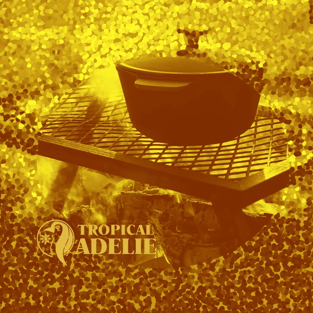 A large cooking pot sits on a metal grill over an open wood fire with visible smoke. The image is presented in a golden monochrome style within a central circle, surrounded by a gold-toned mosaic border. The 'Tropical Adelie' logo is visible in the lower left.