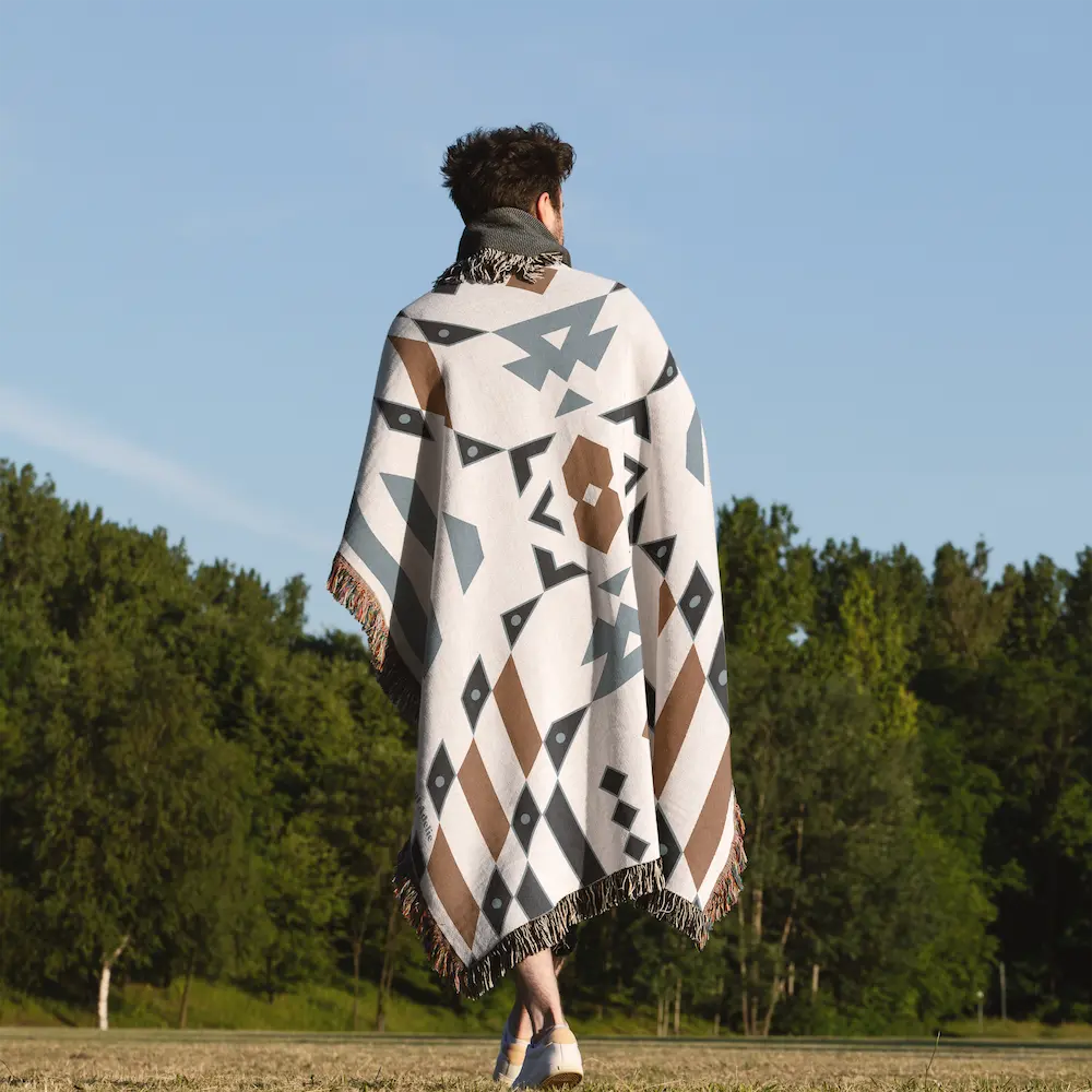 Wandering Warrior Blanket with a geometric pattern in blue, brown, and white worn by a person from behind.