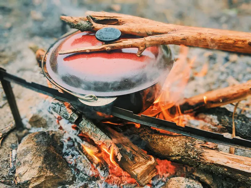 A pot cooking over an open fire on glowing embers, showing the simple setup used for camping food over fire.