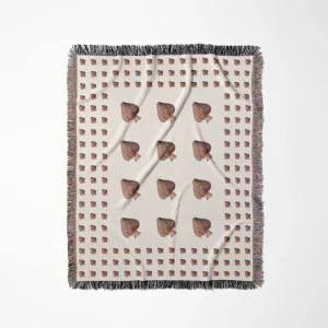 Cream woven throw blanket laid flat on a white background, featuring a grid pattern with mushroom accents and dark fringe trim, shown from a slightly different angle.