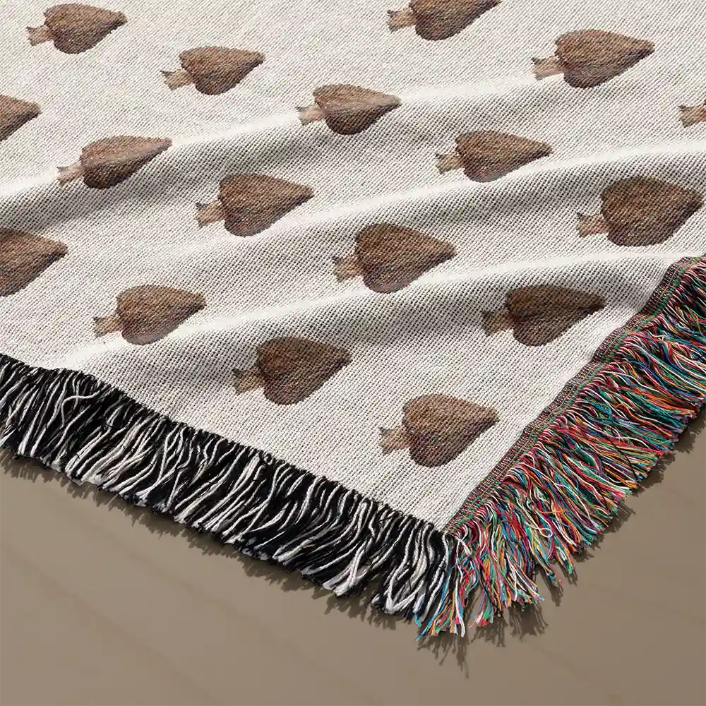 Close-up of the blanket's corner showing brown mushroom motifs and the multicolor woven fringe trim on a light surface.
