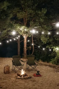 How to make camping comfy — a cozy tent campsite at dusk with warm string lights, a soft blanket, and a lantern glowing by the fire