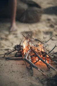 Close-up of a small campfire burning on a sandy beach at a beach campsite